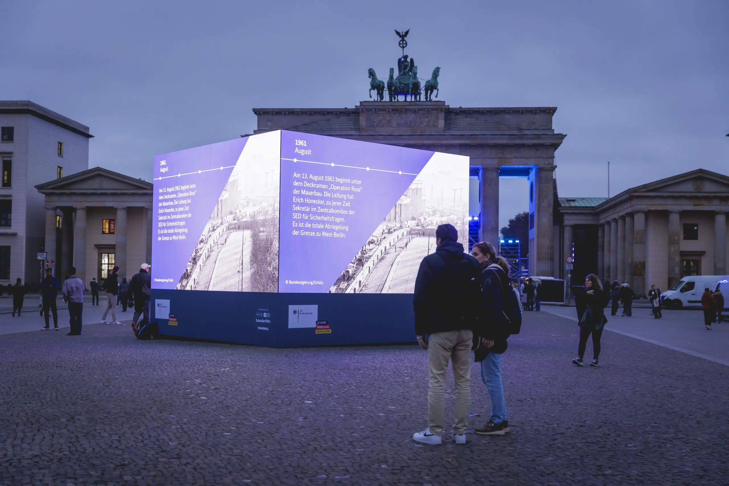 People standing in fornt of a cube made out og screens in front of Brandenburg Gate
